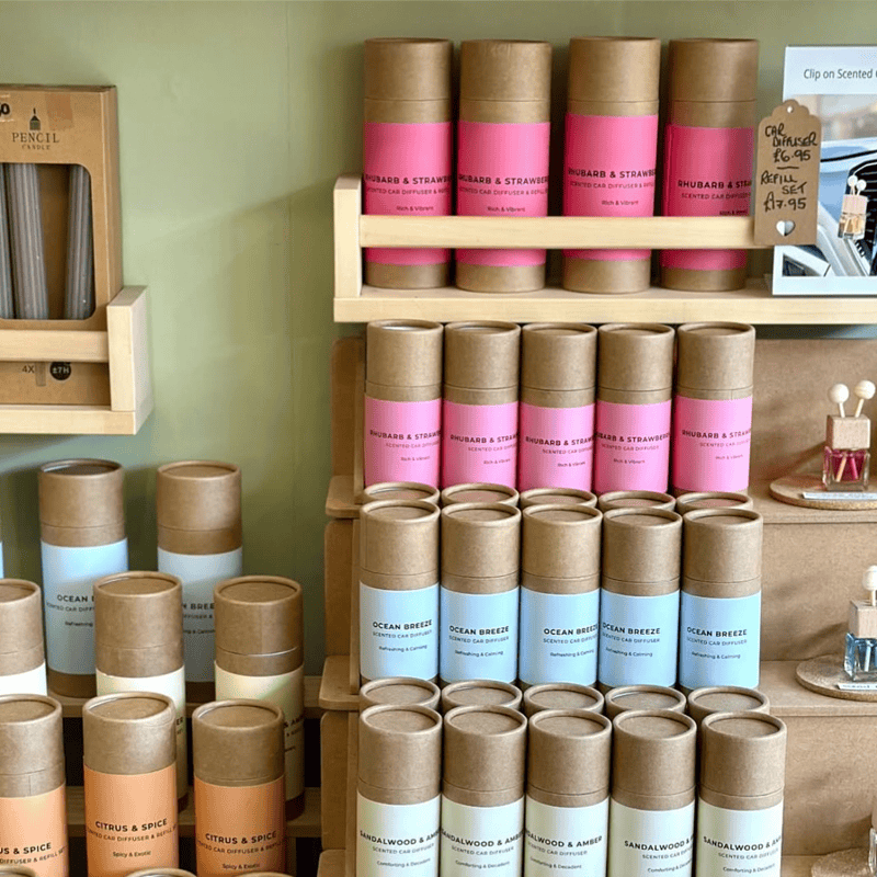 Deluxe luxury car fragrance diffusers in pink, blue, and orange packaging displayed on wooden shelves.